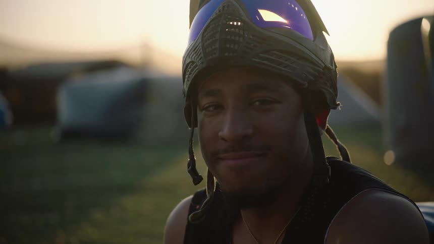 Sun back lights man wearing helmet with goggles as he sits in large multi tent campsite