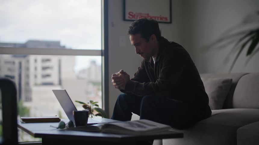 A man is sitting in front of a table as he opens his laptop computer and types