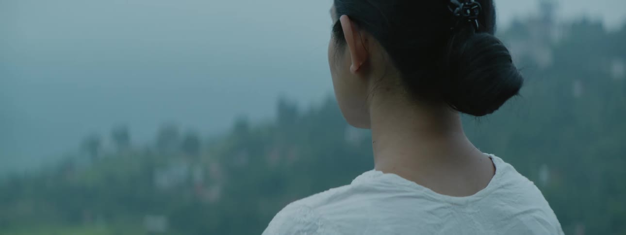 A woman is meditating outside looking down the hill at trees along the coast through the thick fog