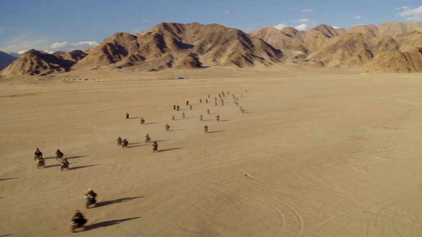 Aerial view of a group of people riding motorcycles through the desert near the mountains at daytime