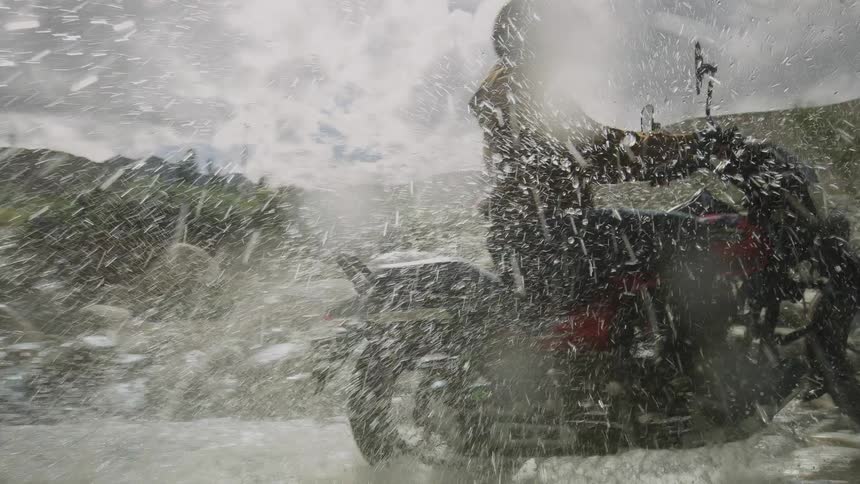 Man riding a motorcycle splashes water whlie crossing a river