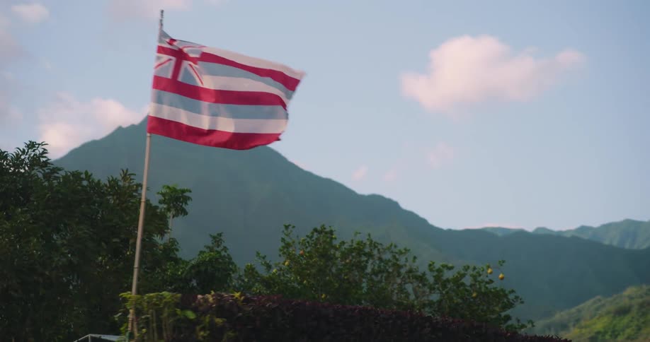 Hawaiian flag waving on a flagpole in front of the mountains at daytime
