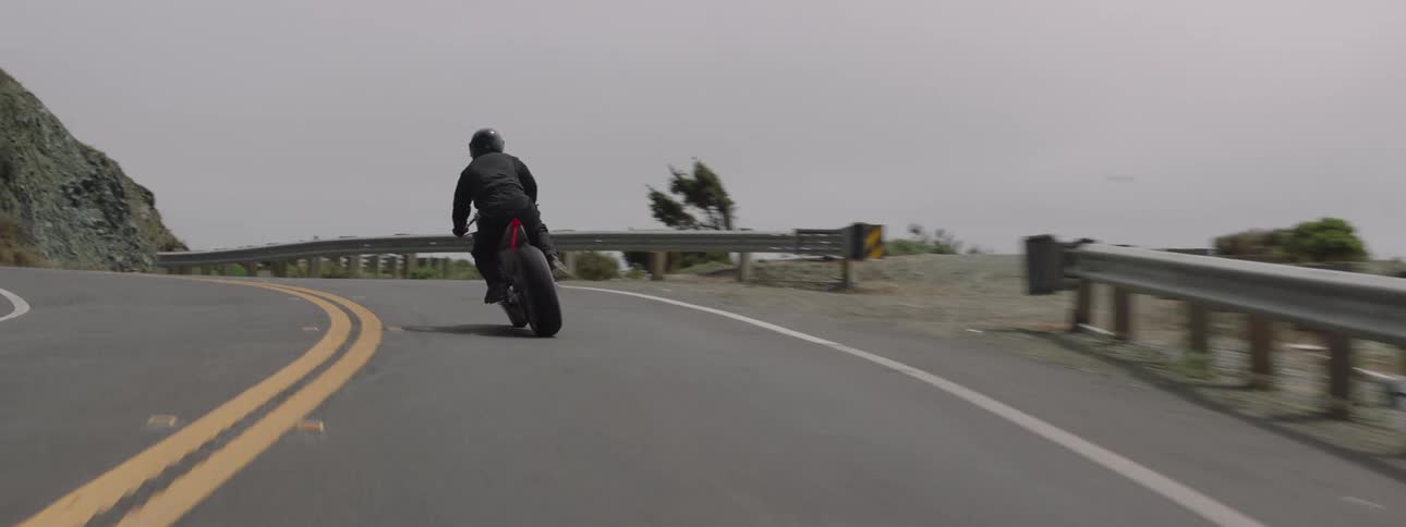 A person rides their motorcycle on the road by the cliff