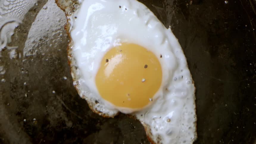 Overhead view frying an egg and sprinkling spices over it