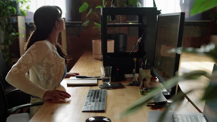 A woman is seen working on her desktop computer while also checking something by her side showcasing her ability to multitask efficiently