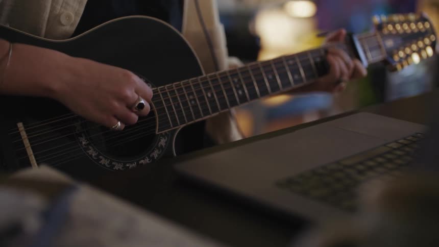 Woman wears headphones and plays guitar while sitting in front of laptop