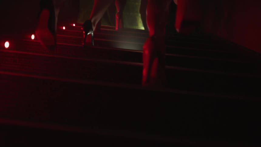 Women in heels walking up stairs lined in lights in dark hallway