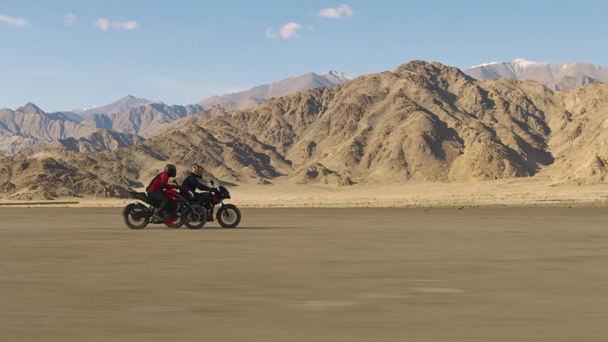 Two people are riding motorcycles near a mountainous area