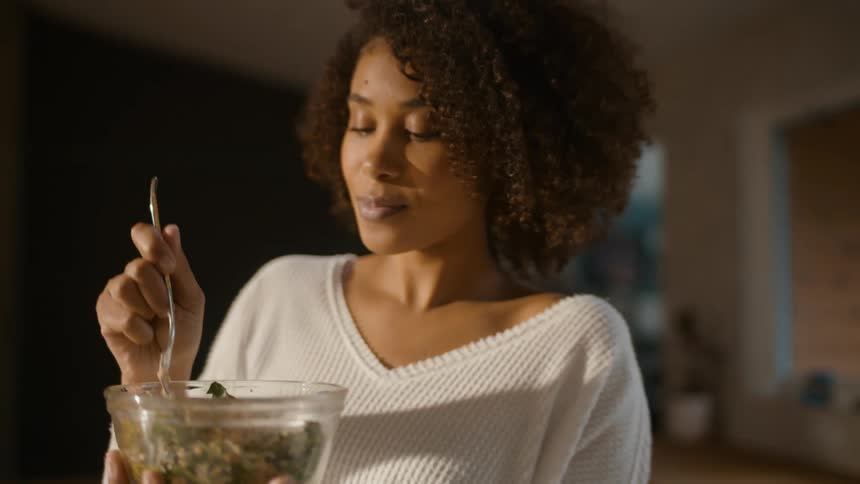 A woman is sitting indoors and eating a salad