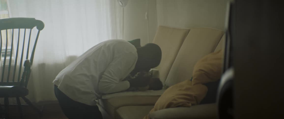 Father kneels and kisses baby lying on couch