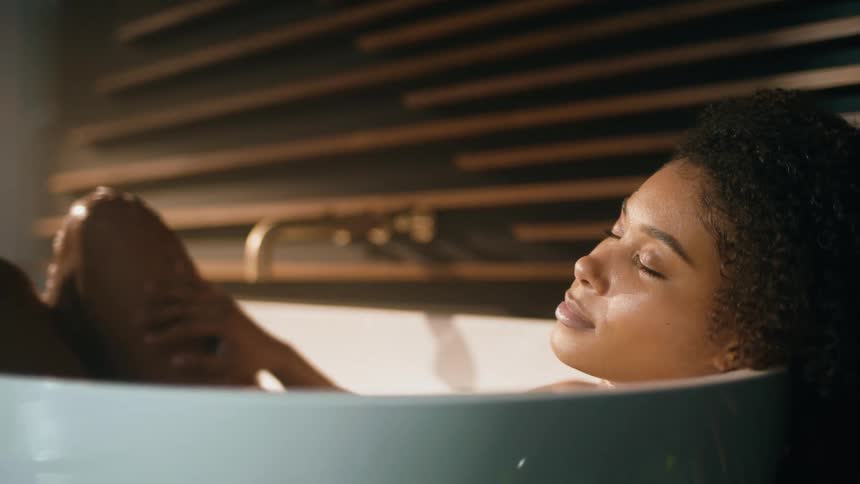 A woman is bathing herself in a bathtub
