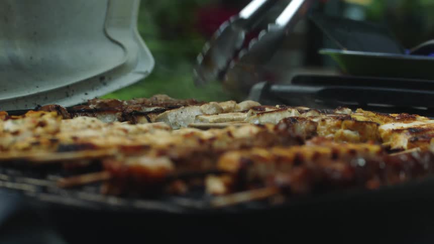 Meat and kebabs being cooked on an outdoor grilled and turned over with tongs