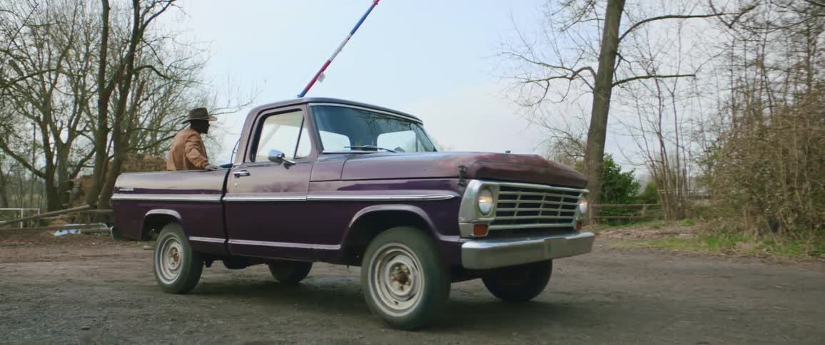 A man is sitting in the back of a pickup truck as it takes off and travels on a country road