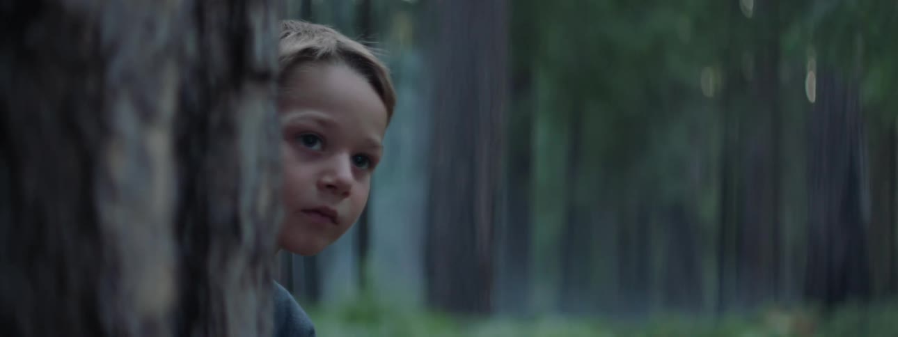 Young boy hiding behind tree and looking around in the forest