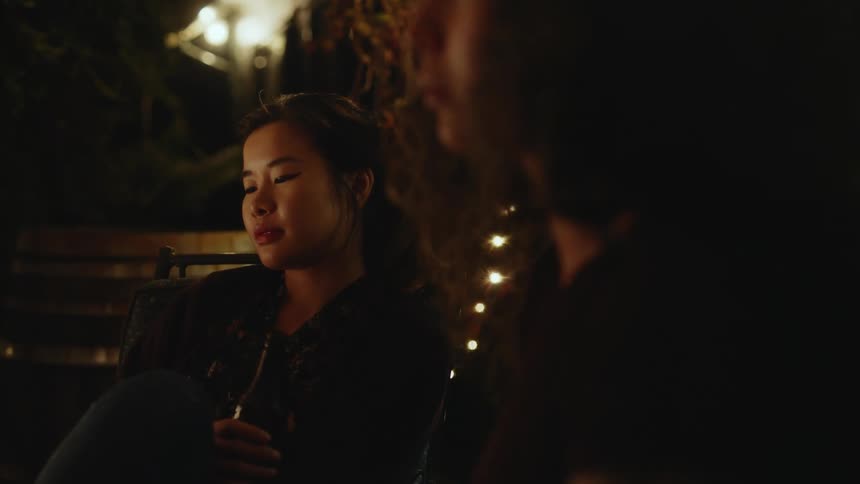 Light shines on a womans face as two people are sitting outside relaxing at night