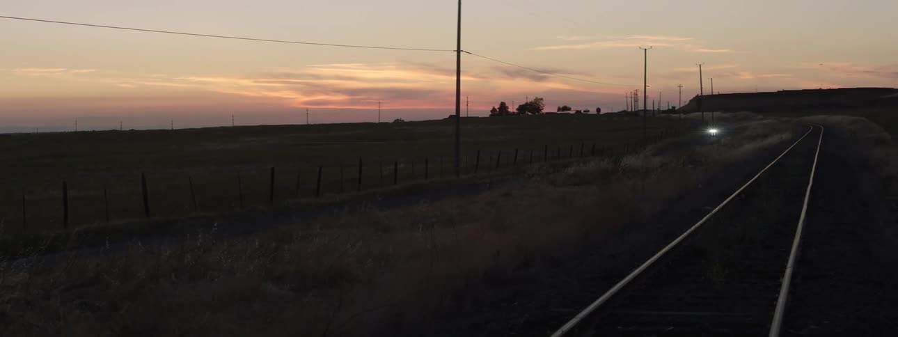 A rural area with a train track and a person on a motorcycle driving down the road at dusk