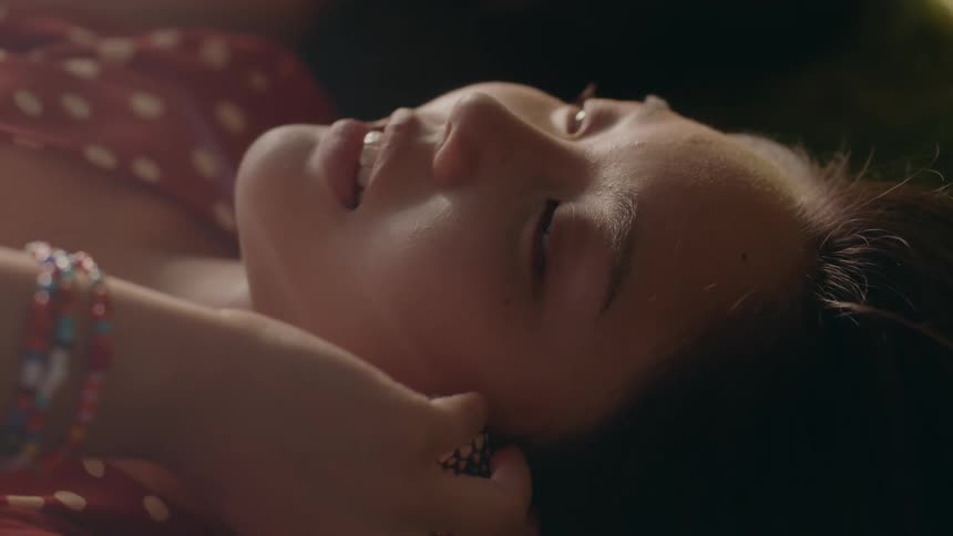 Young woman lying on back while listening to seashell and smiling