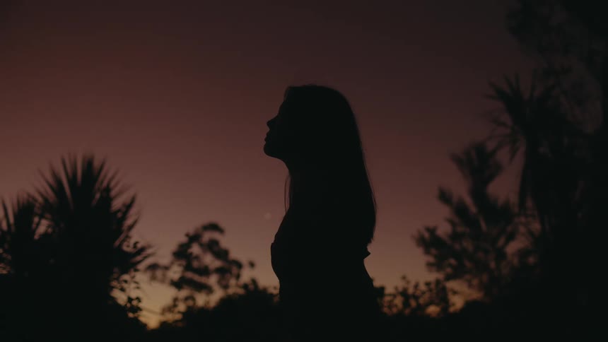 Woman stands silhouetted against a red sky at night