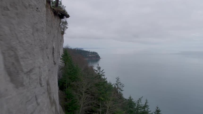 Traverse along the edge of a high sea cliff next to glass calm ocean water