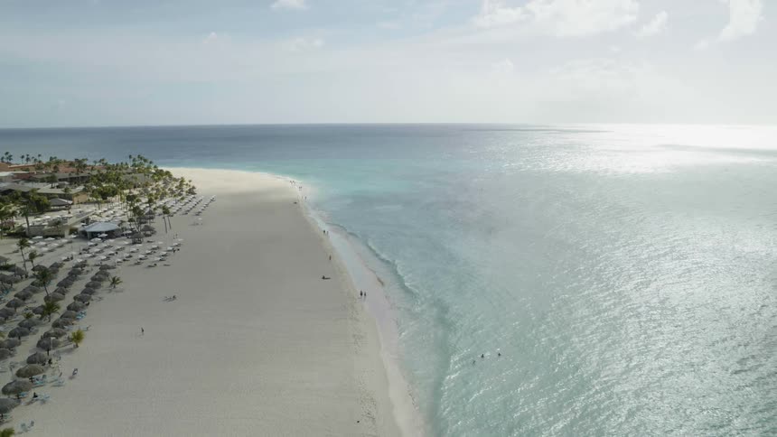 People relax and play in the blue water along a beautiful resort beach as gentle waves wash ashore