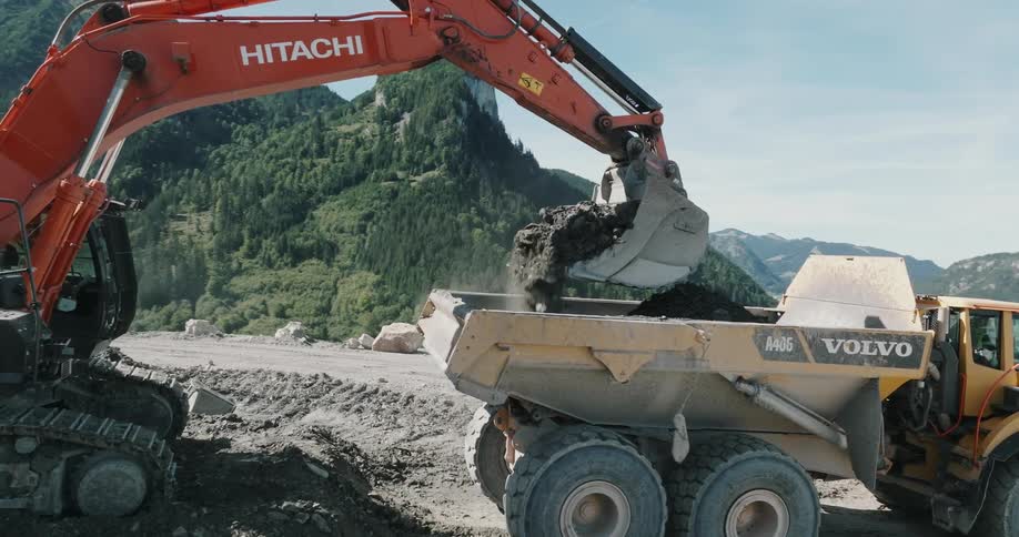 Excavator dumping dirt onto dump truck from mountaintop site