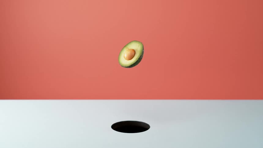 Avocado half with pit falls through hole in white surface