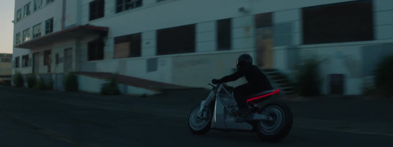 A person passes by the buildings on a motorcycle