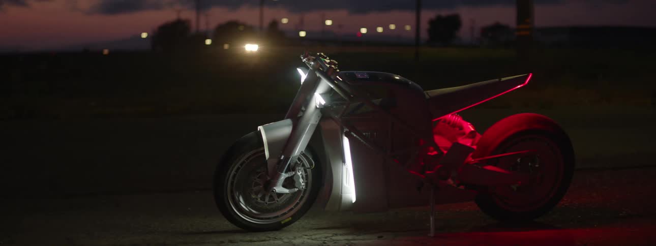 A black and red motorcycle is shown at night sitting on a road with the sky a neighborhood street and lights in the background