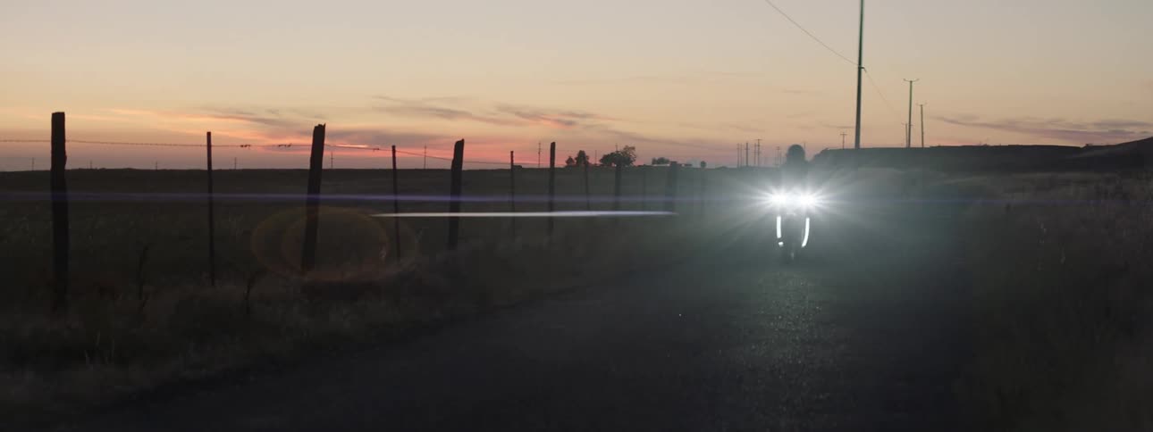 A person is riding their motorcycle through a rural area at dusk