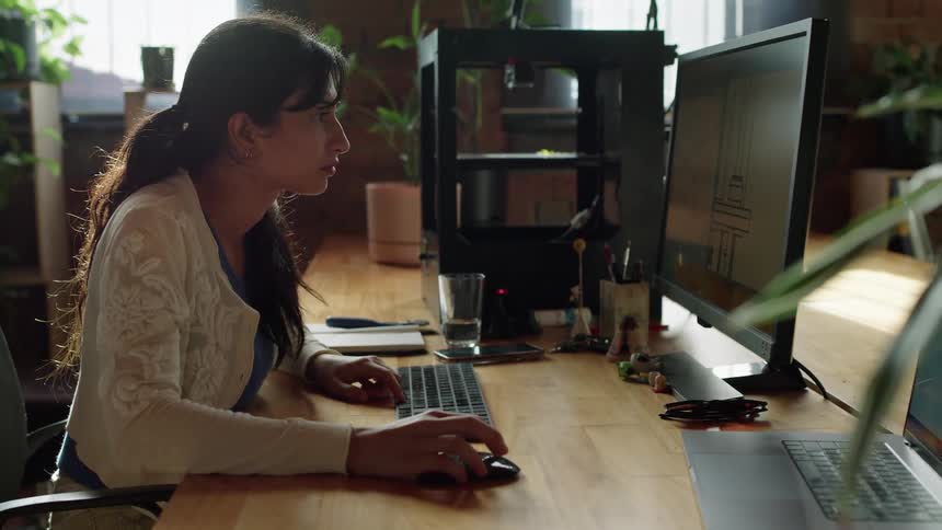 Woman with white shirt and ponytail drinks a glass of water working on computer in the office