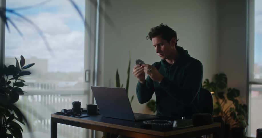 A man is sitting at a desk in front of a laptop computer as he looks at a round wheel gear
