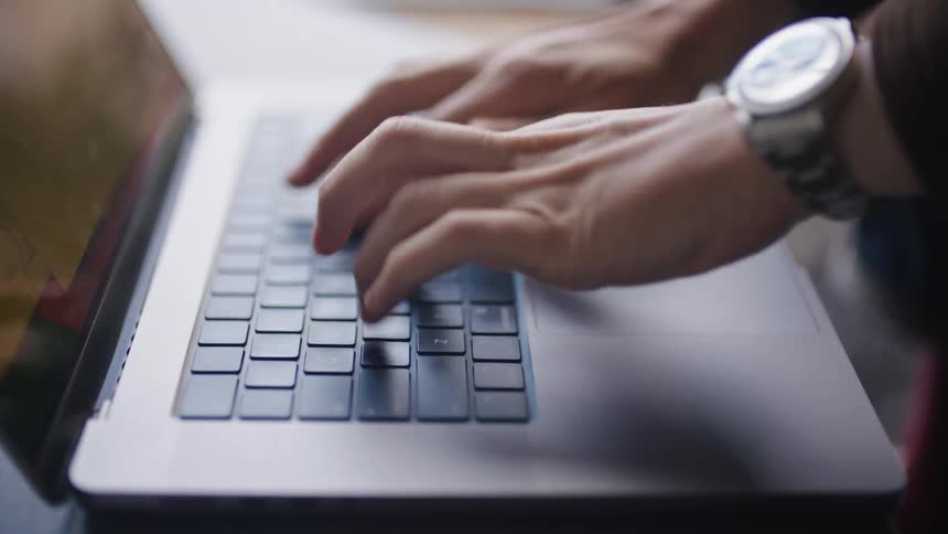 Man with watch and jacket types on laptop