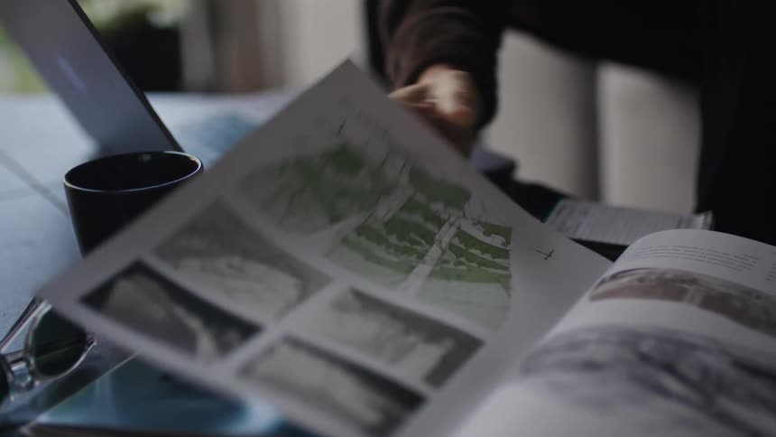 A man flips through a couple of book pages and types on his laptop