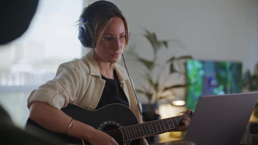 A woman is playing her guitar with headphones on