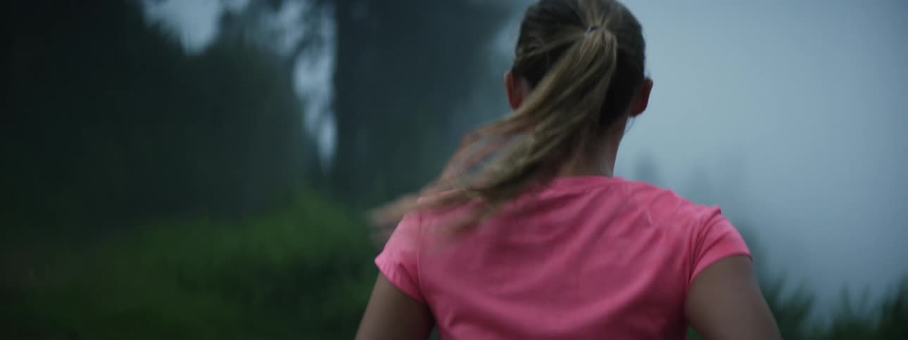 A girls ponytail swings as she runs on a foggy road