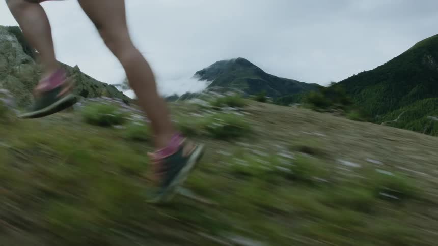 Close up of the legs of a woman running uphill on the slope of a mountain at daytime