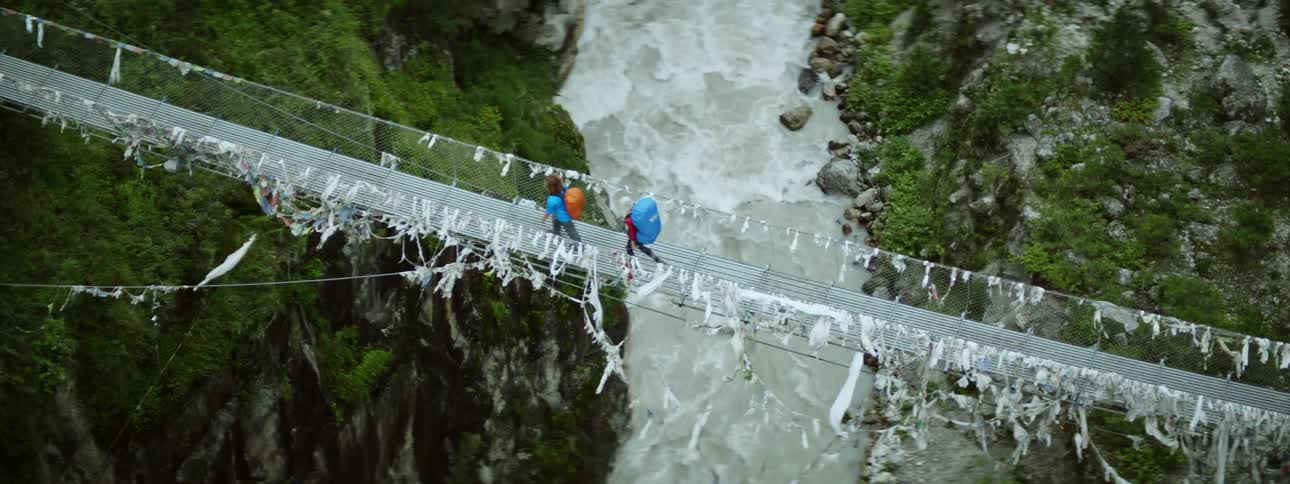 People crossing a thin bridge over a rocky tropical river