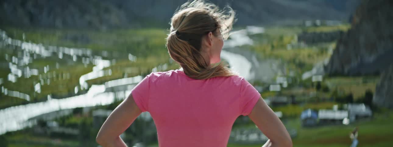 A woman running and then stopping and looking out over a valley with water running through it