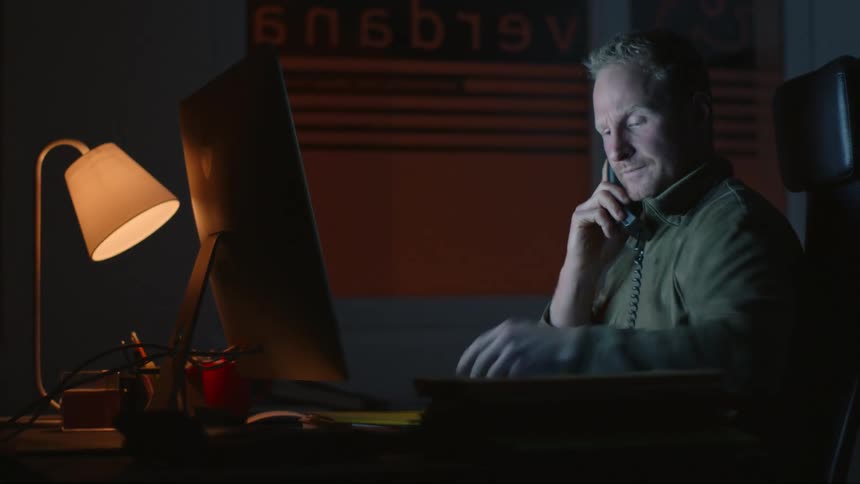 A man sitting at his desk talking on the phone shuffling through papers and looking at them