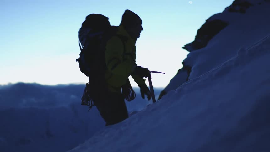 A man is hiking up a mountain during the winter