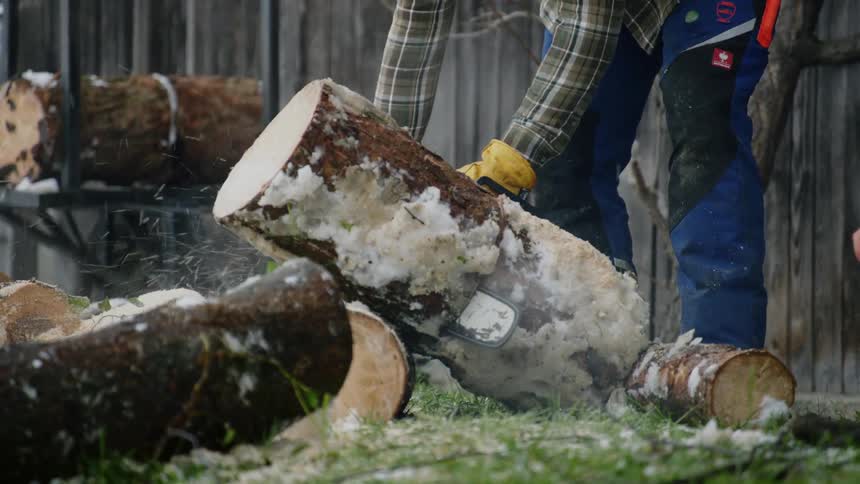 A man is standing outside cutting wood logs with a chainsaw