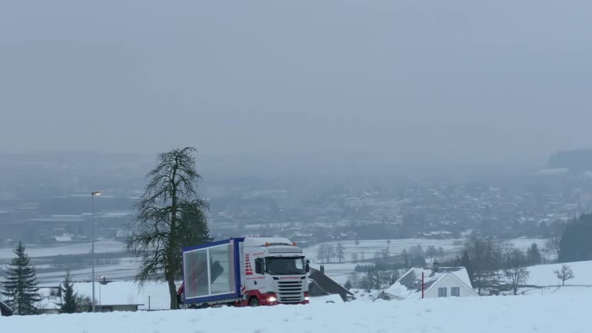 A snowy landscape showing a couple houses in the suburbs with a truck driving by on the road