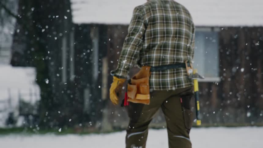 Man wearing tool belt walking outdoors while its snowing