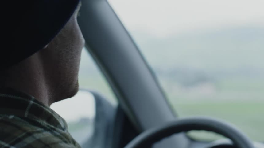 A close up of a mans face looking around as he drives a car