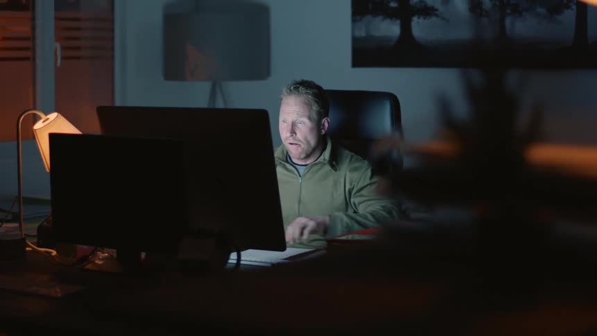 Late Night Work Stress: Man in Black Chair Analyzing Papers on Large Screen