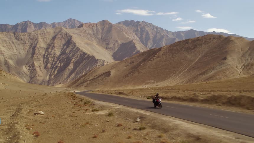 A motorcycle travels on a desert road with mountains in the distance