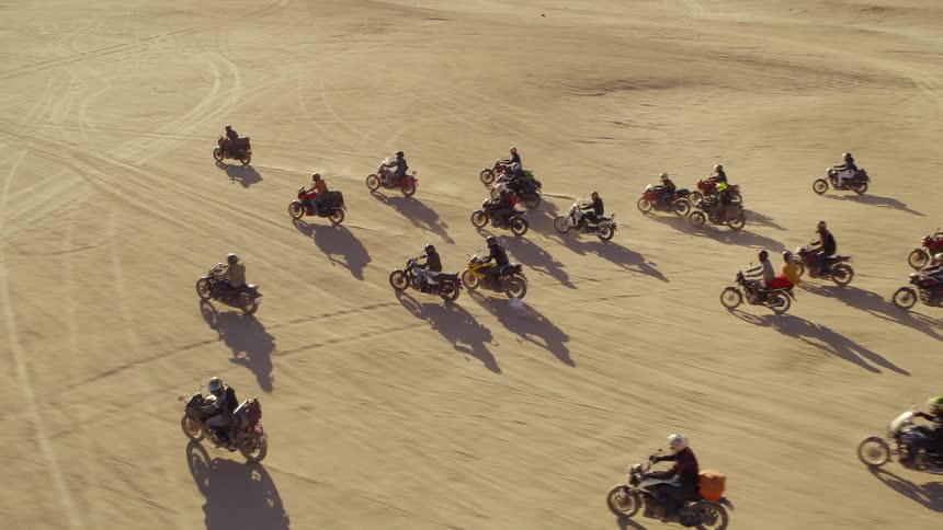 A large group of motorcyclists ride through an empty desert