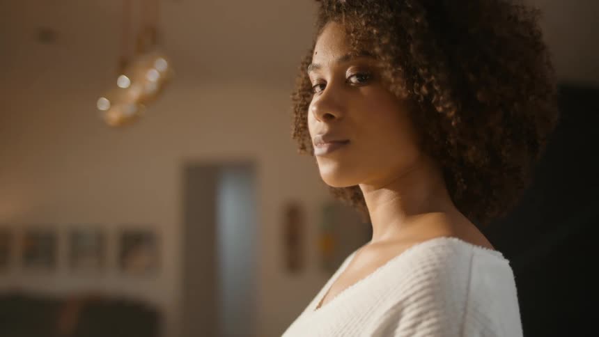 A woman is standing in a room as she turns her head and looks with a slight smile on her face