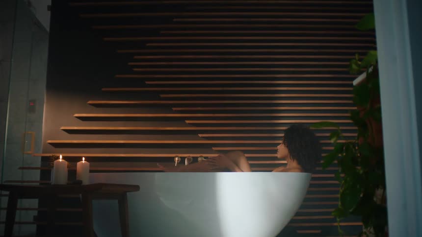 Woman with curly hair lies in bathtub in the bathroom