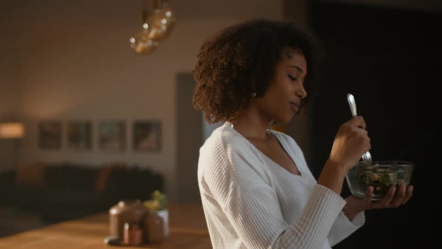 A woman is eating a salad in the kitchen